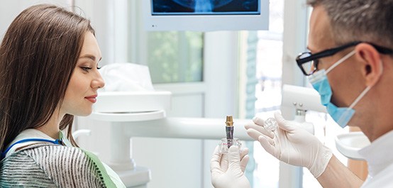 Dentist showing sample dental implant to woman in dental chair