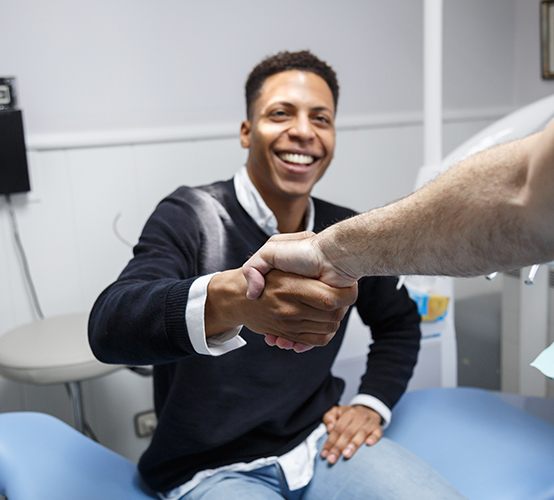 Man in dental chair shaking hands with dentist