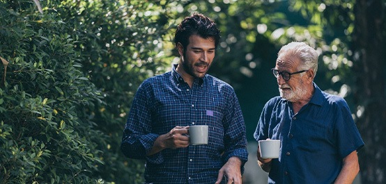 Older man in blue shirt talking to younger man in blue checkered shirt outside