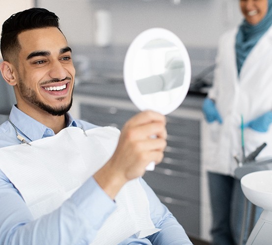 a man sitting in a dental chair and holding a handheld mirror