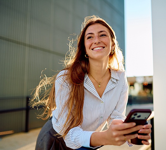 a smiling woman holding a phone and resting on a handrail