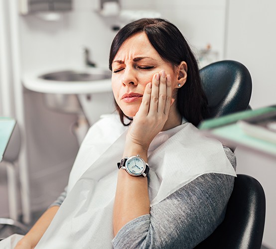 Woman at dental office for emergency dentistry holding jaw in pain