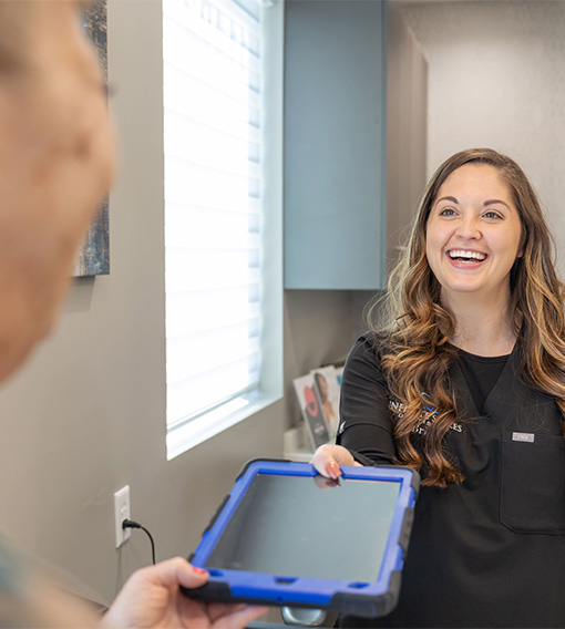 Smiling Owasso dental team member handing a patient a tablet