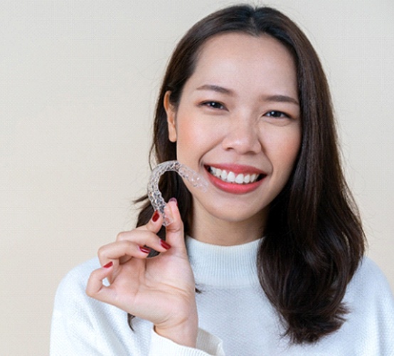 woman smiling and holding Invisalign aligner