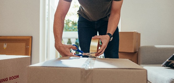 Male using scissors to cut tape while packing box