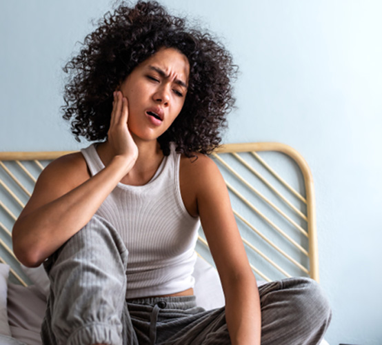 a woman holding her mouth in pain while sitting on her bed