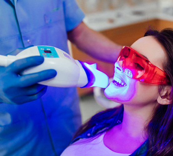 Woman in protective goggles undergoing professional teeth whitening with dentist
