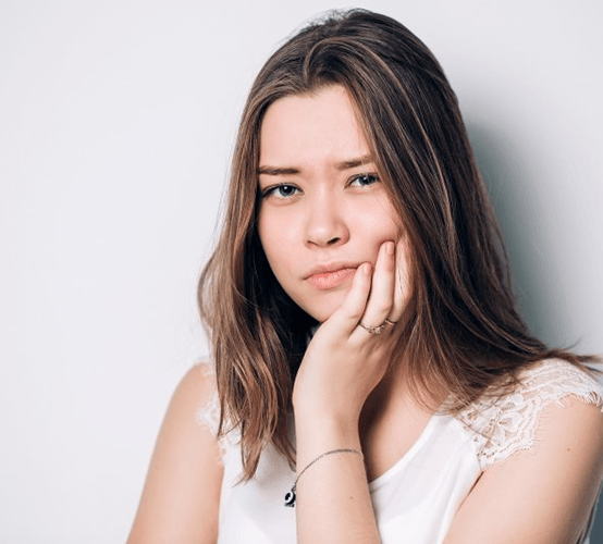 a woman holding her cheek due to impacted wisdom teeth 