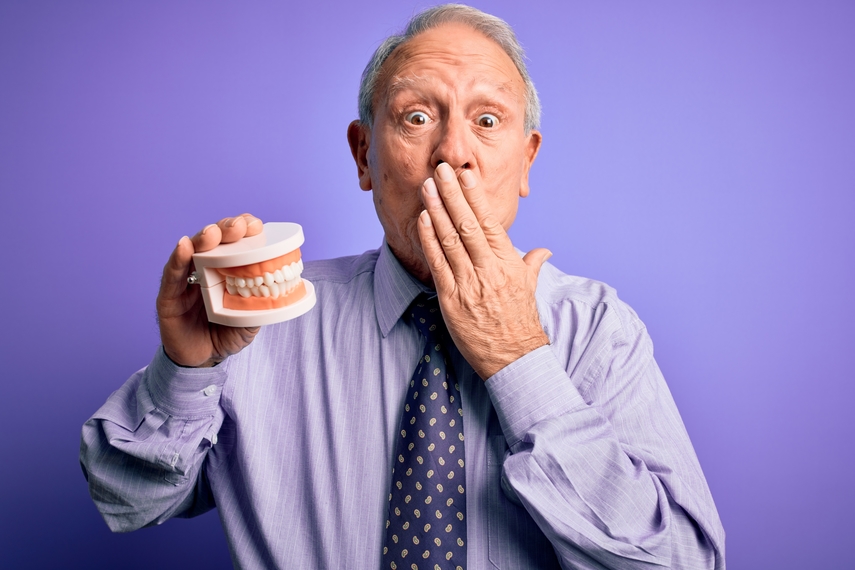 older man holding dentures with hand over mouth