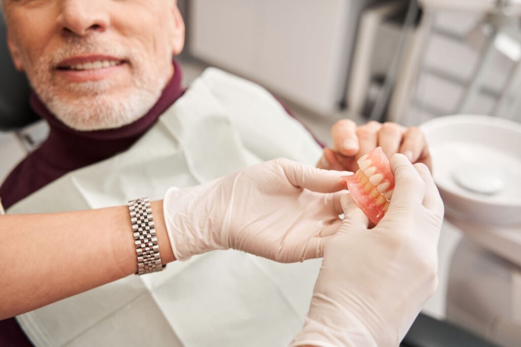Dentist handing dentures to man in dental chair